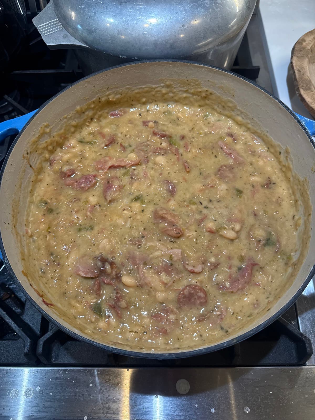 A pot of creamy white beans with sliced andouille sausage simmering on the stove