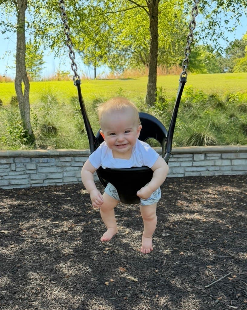 Parker, grinning in a park swing on a sunny day